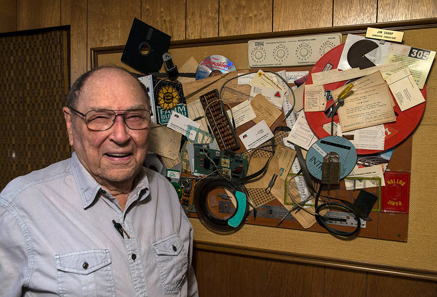 Jim Sharp in 2017 at home, next to a collage of materials representing his years of work as head of Information Technology for Farm Bureau in Manhattan, KS.